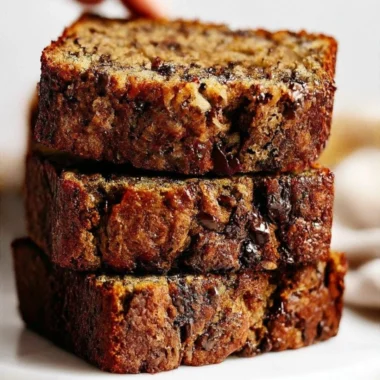 A slice of chocolate chip banana bread on a wooden table, showcasing its moist texture.