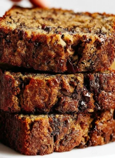 A slice of chocolate chip banana bread on a wooden table, showcasing its moist texture.