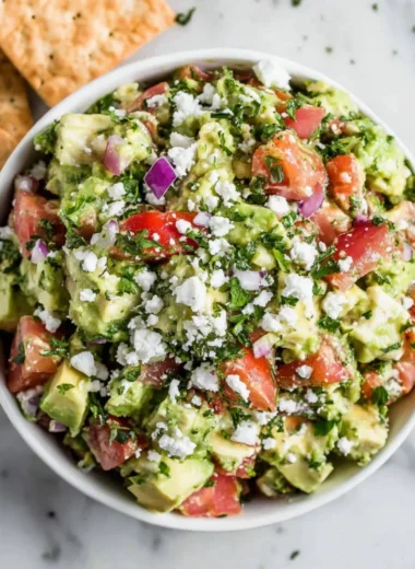 Easy avocado feta dip served in a bowl with fresh herbs and vegetables