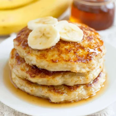 Fluffy banana pancakes stacked with syrup and fresh bananas on top.