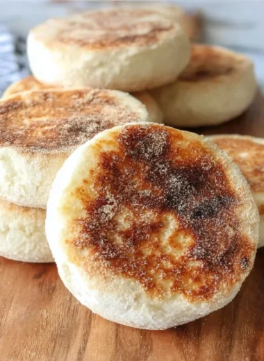 Freshly baked sourdough English muffins stacked on a wooden table.