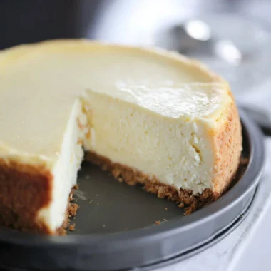 Slice of creamy cheesecake topped with fresh strawberries on a dessert plate.