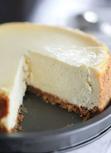 Slice of creamy cheesecake topped with fresh strawberries on a dessert plate.