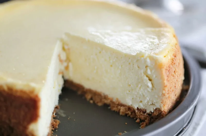 Slice of creamy cheesecake topped with fresh strawberries on a dessert plate.