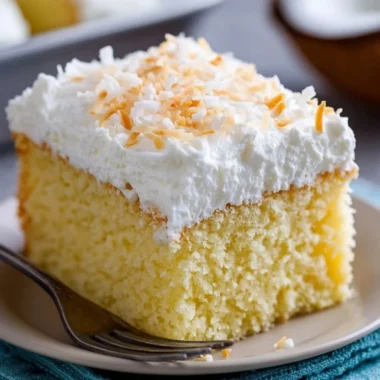 A delicious slice of Coconut Cloud Cake topped with coconut flakes and whipped cream