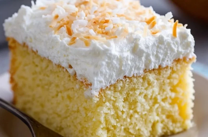 A delicious slice of Coconut Cloud Cake topped with coconut flakes and whipped cream