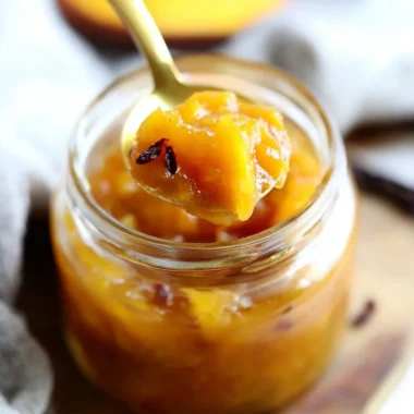Homemade Mango Chutney in a jar with spices and fresh mangoes.