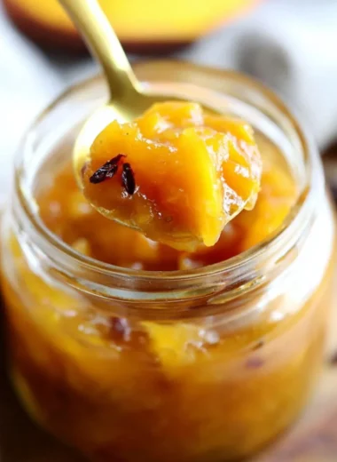 Homemade Mango Chutney in a jar with spices and fresh mangoes.