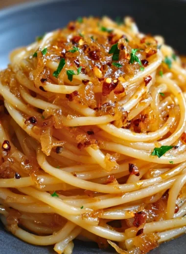 Plate of caramelized onion pasta drizzled with chili oil, garnished with herbs