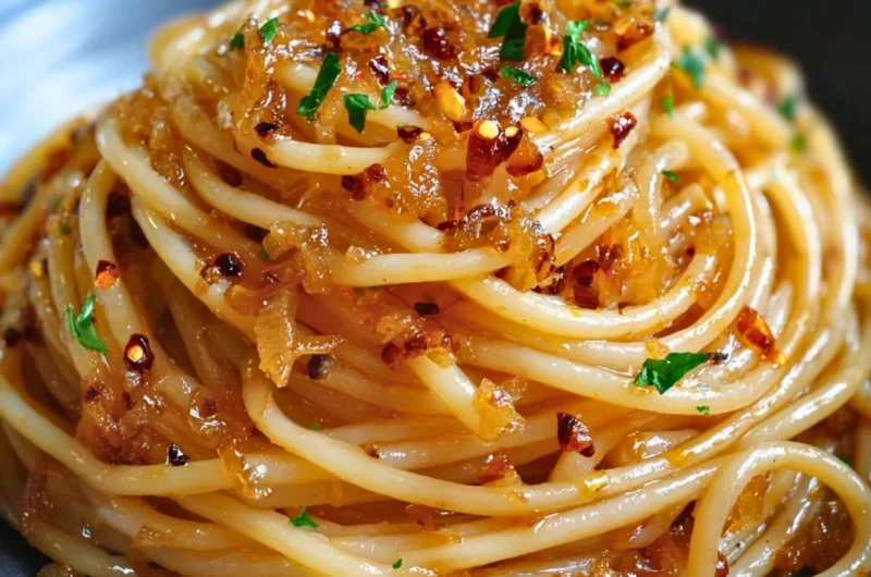 Plate of caramelized onion pasta drizzled with chili oil, garnished with herbs