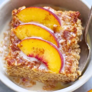 Baked peach oatmeal served in a bowl with fresh peach slices on top