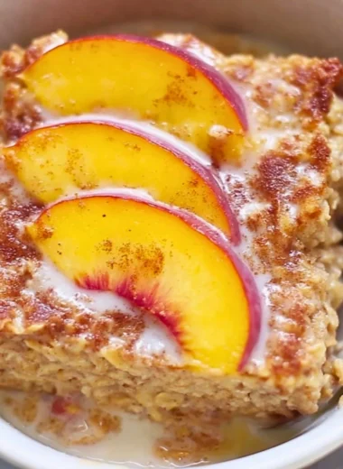 Baked peach oatmeal served in a bowl with fresh peach slices on top