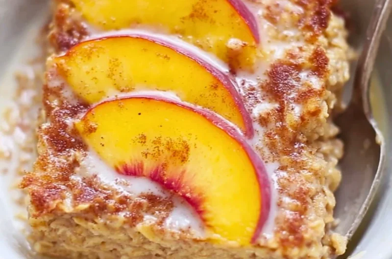 Baked peach oatmeal served in a bowl with fresh peach slices on top