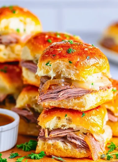 Delicious French Dip Sliders with beef, cheese, and au jus in a serving platter.
