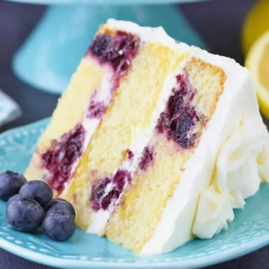 Slice of moist Lemon Blueberry Cake topped with fresh blueberries and lemon zest.