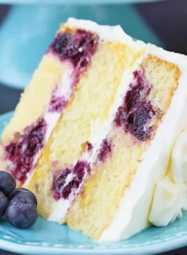 Slice of moist Lemon Blueberry Cake topped with fresh blueberries and lemon zest.