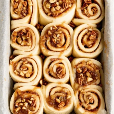 Freshly baked apple pecan cinnamon rolls topped with icing on a plate.