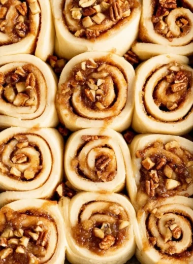 Freshly baked apple pecan cinnamon rolls topped with icing on a plate.