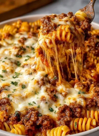 Cheesy baked beef rotini topped with melted cheese and herbs in a baking dish.