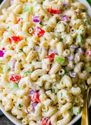 Creamy macaroni salad in a bowl with fresh vegetables and dressing