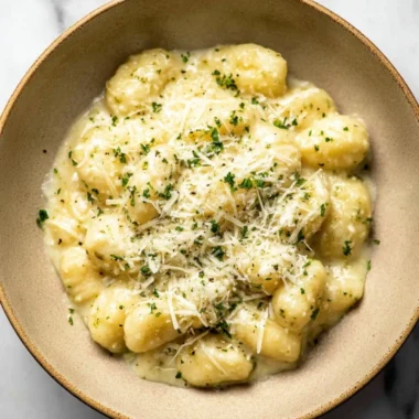 Creamy pesto gnocchi with fresh basil and cheese, served in a bowl.