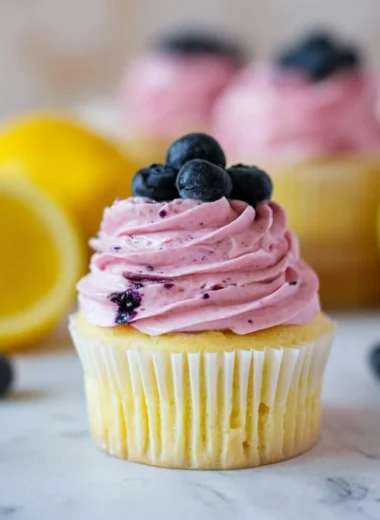 Lemon cupcakes topped with blueberry buttercream on a rustic table.
