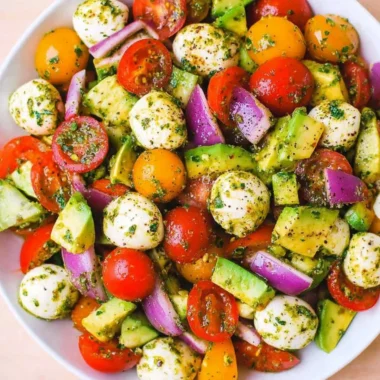 Tomato Cucumber Salad with Avocado, Mozzarella, and Basil Pesto served in a bowl