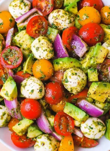 Tomato Cucumber Salad with Avocado, Mozzarella, and Basil Pesto served in a bowl