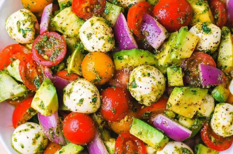 Tomato Cucumber Salad with Avocado, Mozzarella, and Basil Pesto served in a bowl