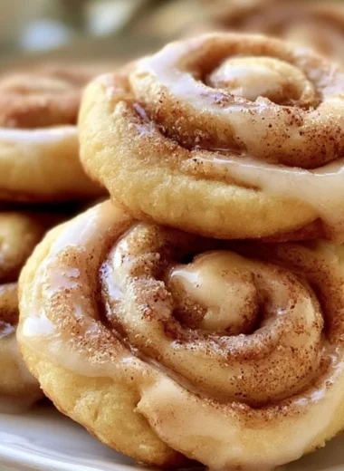 Freshly baked cinnamon roll cookies topped with icing and a sprinkle of cinnamon.