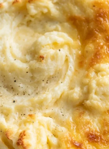 Creamy baked mashed potatoes in a casserole dish topped with golden brown cheese