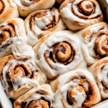 Freshly baked apple pie cinnamon rolls topped with icing and cinnamon.