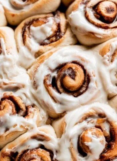 Freshly baked apple pie cinnamon rolls topped with icing and cinnamon.