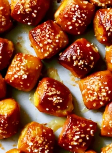 Homemade soft pretzel bites served with dipping sauce on a wooden platter.