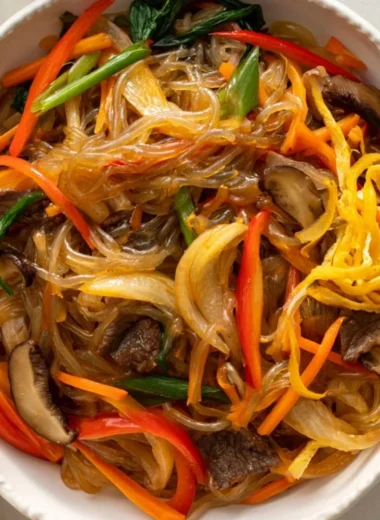 A vibrant plate of Korean Japchae with stir-fried noodles and colorful vegetables.