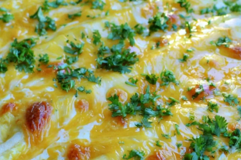 Overnight breakfast burrito casserole topped with cheese and fresh herbs