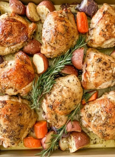 Cozy sheet pan chicken thighs with herbs and roasted vegetables on a baking tray.